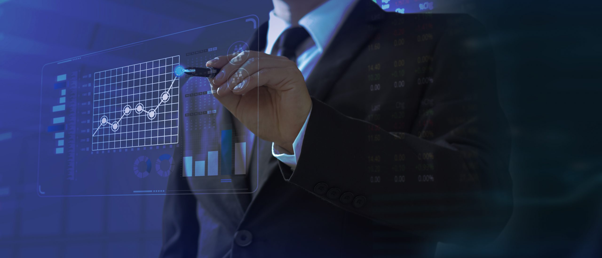 A suited businessman uses a pen to touch a glowing holographic dashboard of line, bar and pie charts with stock data